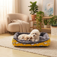 Panier douillet jaune à motifs pour chiens et chiots dans un salon moderne, avec un Bichon Frise et un Cavalier King Charles Spaniel blottis ensemble.