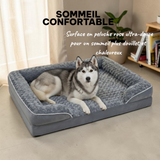 Husky sibérien gris et blanc allongé dans un grand panier orthopédique gris avec surface en peluche ultra-douce et rebords rembourrés, dans un salon lumineux - sommeil douillet et chaleureux