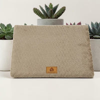 Lit orthopédique beige Happy Animalia en tissu bouclette texturé avec badge cuir, entouré de plantes succulentes sur fond blanc.