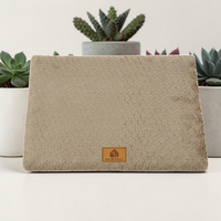 Lit orthopédique beige Happy Animalia en tissu bouclette texturé avec badge cuir, entouré de plantes succulentes sur fond blanc.