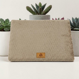 Lit orthopédique beige Happy Animalia en tissu bouclette texturé avec badge cuir, entouré de plantes succulentes sur fond blanc.