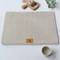 Lit orthopédique gris clair Happy Animalia en tissu bouclette texturé avec badge cuir, entouré de plantes succulentes sur fond blanc.
