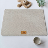 Lit orthopédique gris clair Happy Animalia en tissu bouclette texturé avec badge cuir, entouré de plantes succulentes sur fond blanc.
