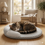 Chat tigré endormi paisiblement sur un coussin orthopédique rond gris et blanc posé sur un parquet de salon lumineux.